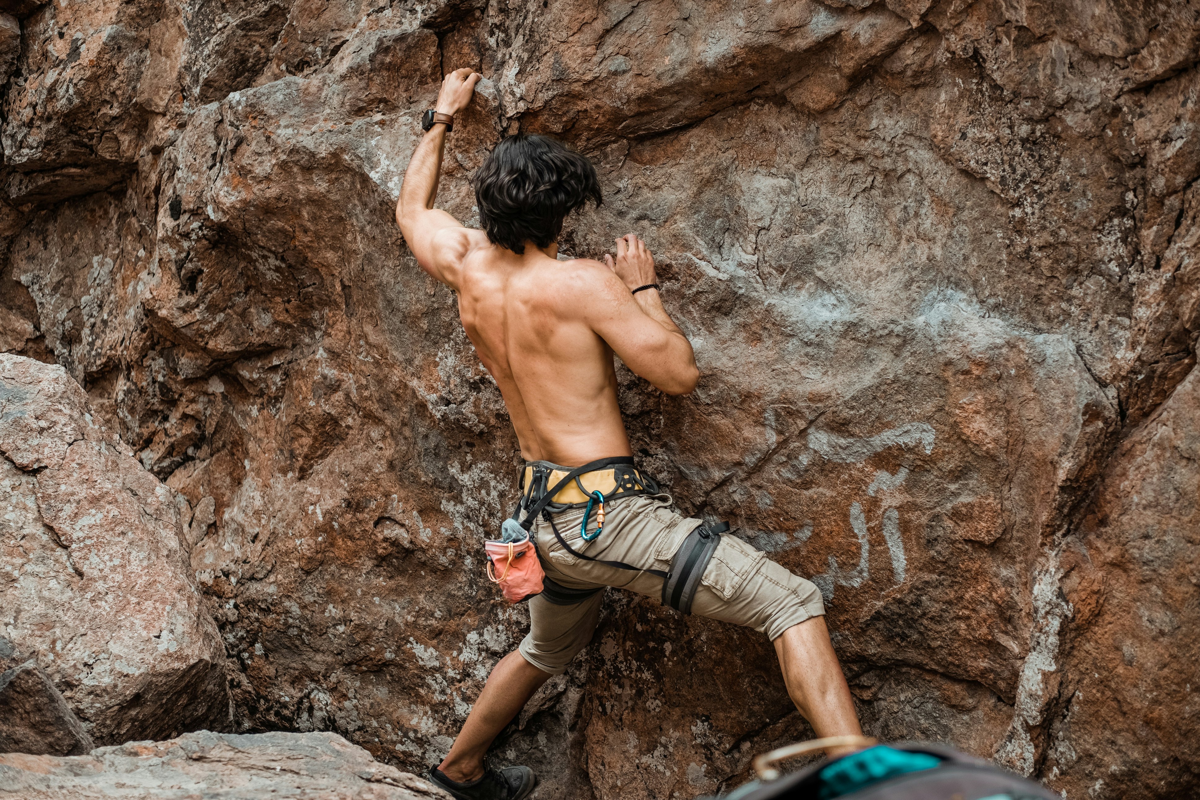 topless man climbing on brown rock formation during daytime